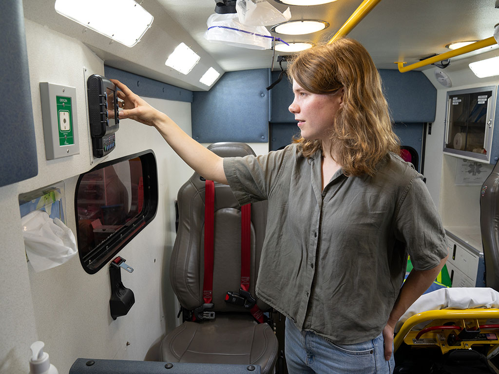 Abigail Schipper presses buttons on a mounted device inside the packed ambulance.