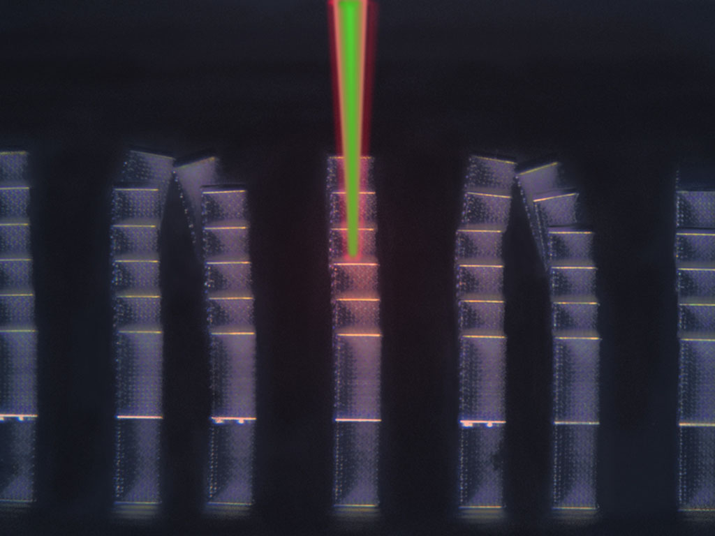 Seven tall, rectangular columns stand against a black background. The columns are made of a lattice-like pattern and some of them tilt at the top. In the center of the image, a green beam of light reaches between the top of the image and the middle column