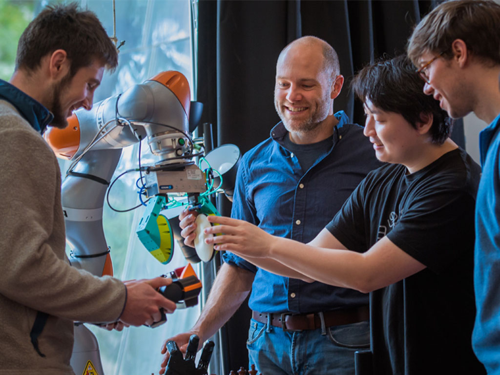 Professor Russ Tedrake (second from left) examines a robotic arm with students from 6.800 (Robotic Manipulation). Tedrake designed the course in response to the growing need for engineers to survey the latest advancements in robotics while gaining experie