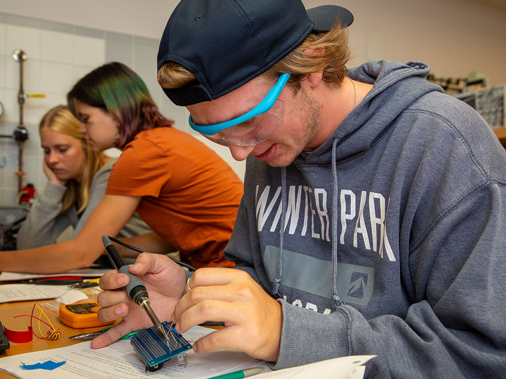 Carter Tucker works on solders a wire as part of a 2.678 Lab assignment