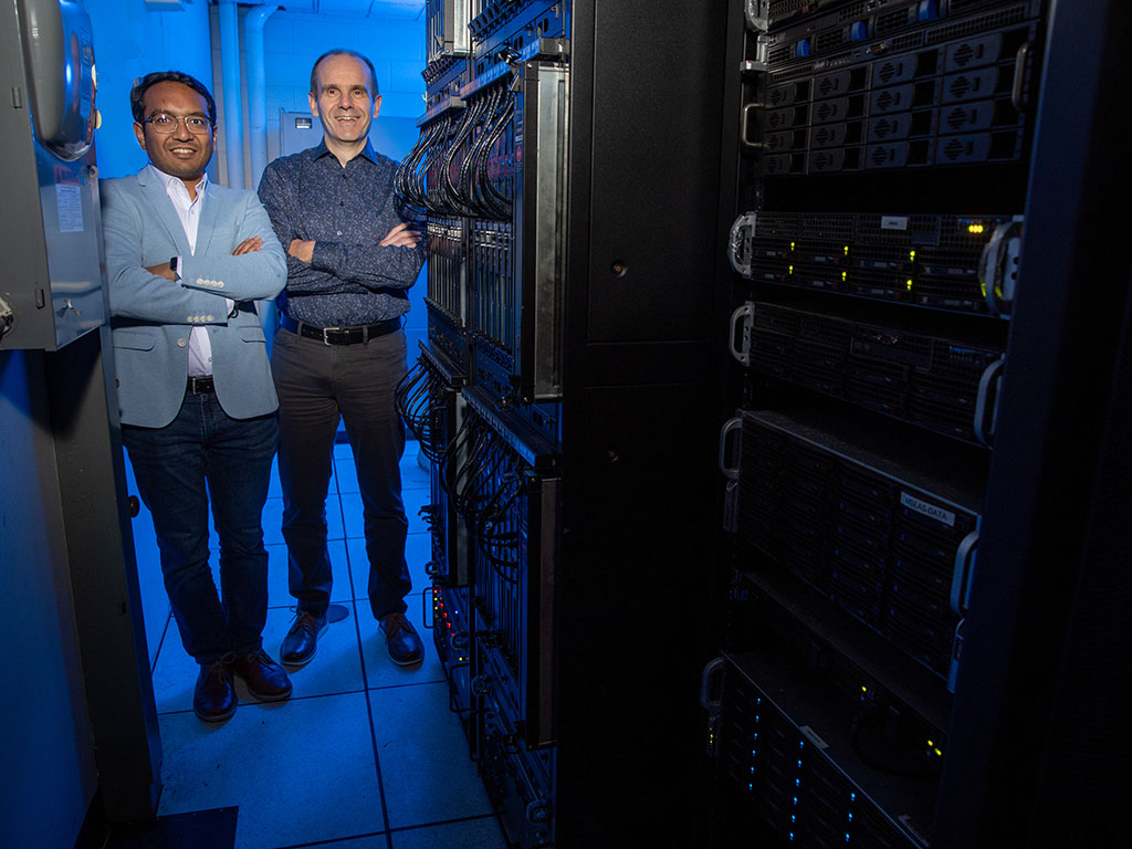 Researchers stand next to large computing devices in a lab at MIT