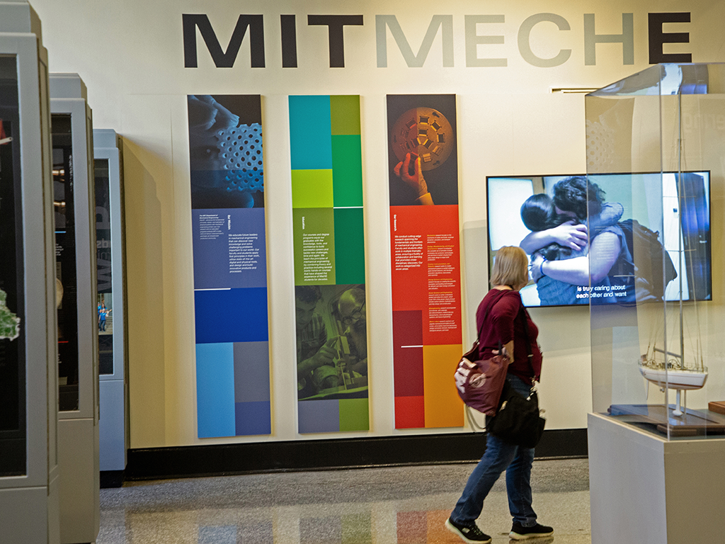 An image of the Hart Gallery, with MIT MechE in large letters and a woman looking at the displays.