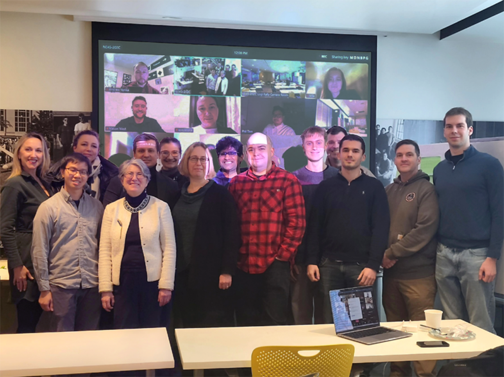 A group of young people in front of a screen displaying zoom tiles with additional people