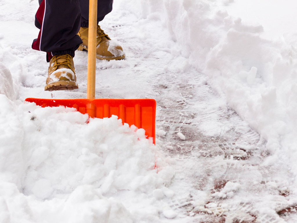 A person in boots shovels snow on a sidewalk.