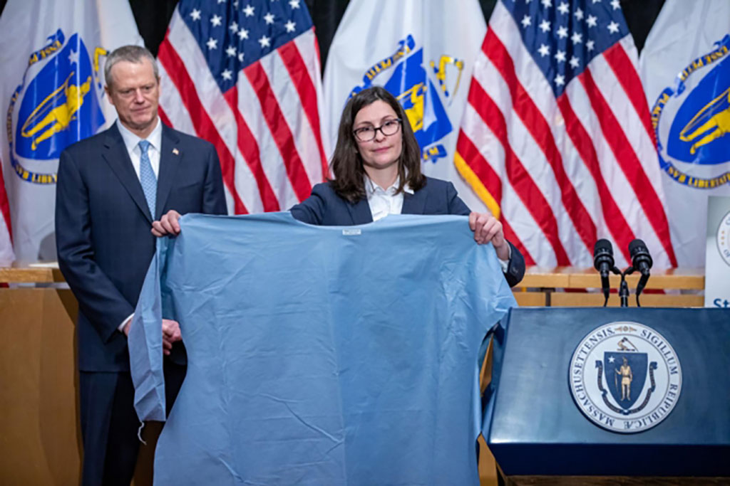 This photo, from April 13, 2020, shows Gov. Charlie Baker, left, and Brenna Schneider, CEO of 99Degrees, who holds one of the hundreds of thousands of medical isolation gowns her company has produced with support from M-ERT.