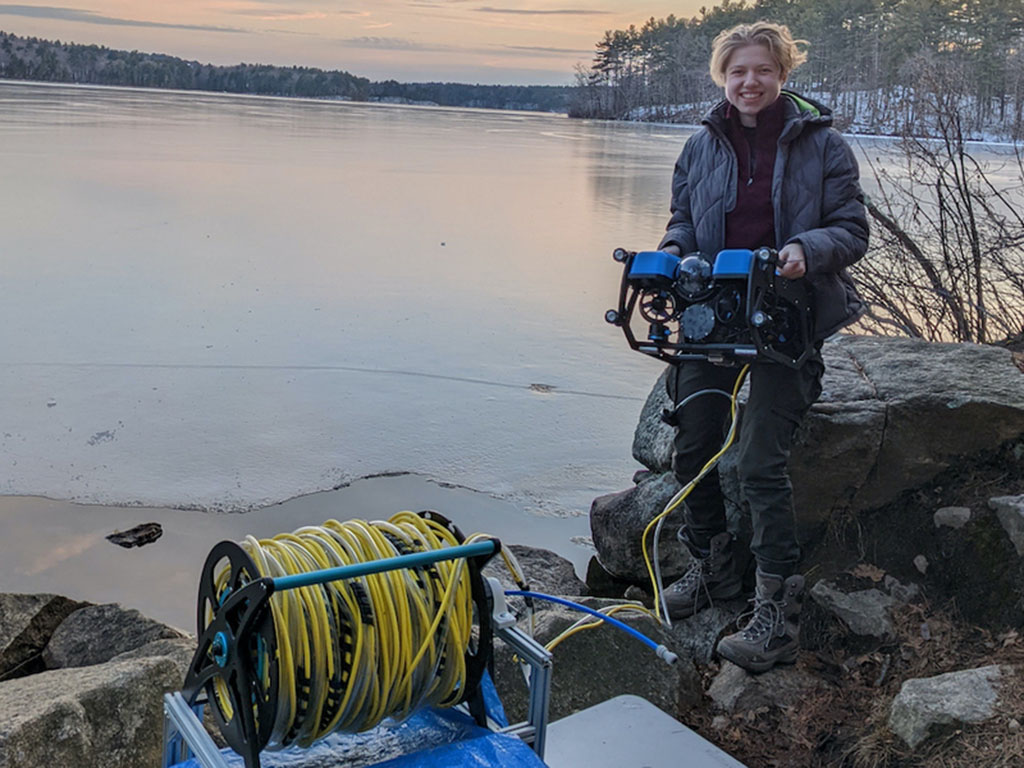 Sylas Horowitz stands by the edge of a lake holding their remotely operated vehicle.