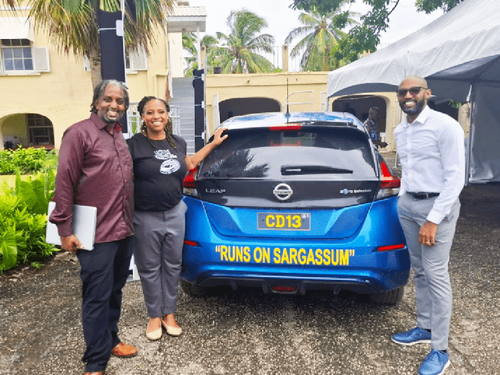 Legena Henry, CEO and cofounder, stands next to a sargassum-powered vehicle during a recent test drive, along with Nigel Henry, cofounder and managing director (left), and Lorenzo Hodges, technical advisor (right).