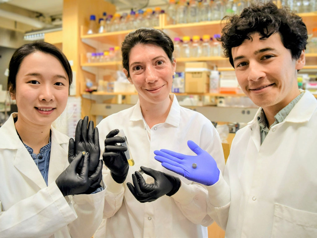 Qijun Liu, Maria Eugenia Inda, and Miguel Jimenez, all in lab coats and nitrile gloves, pose with prototypes of a pill-like capsule and a glass vial with yellow liquid