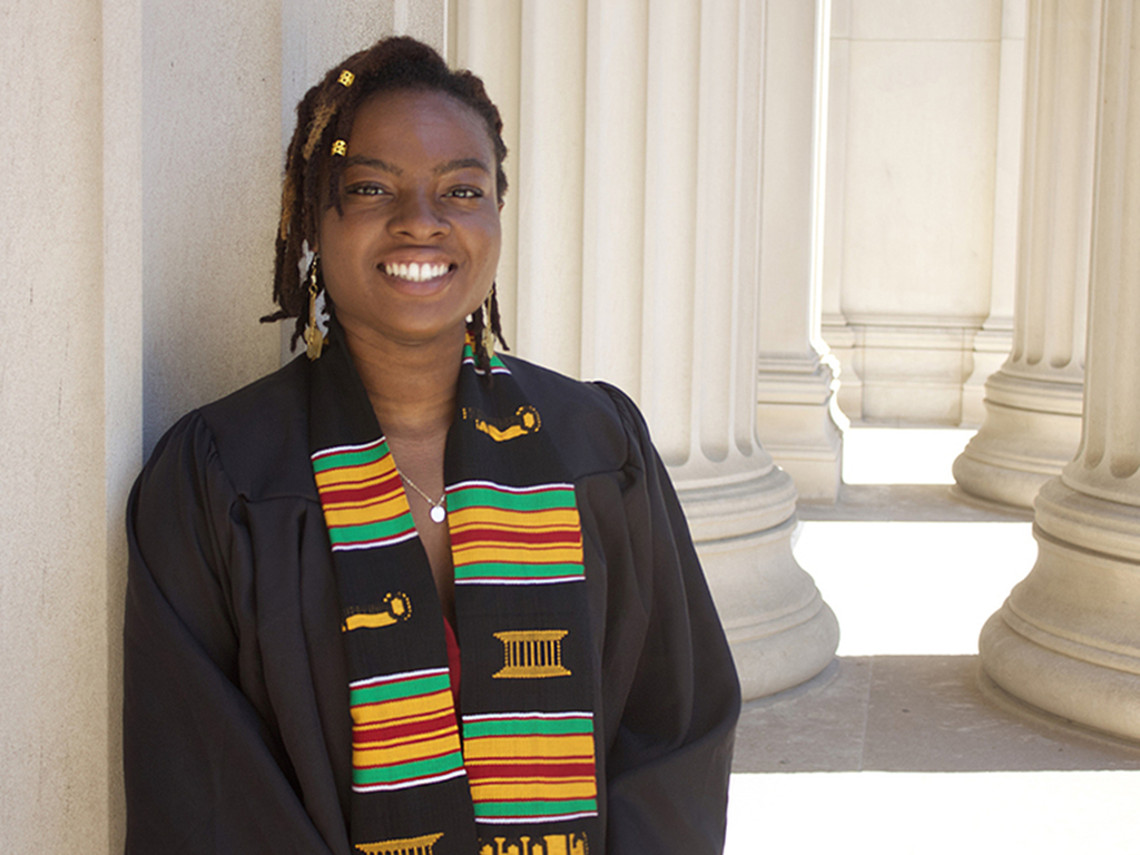 Stacy Godfreey-Igwe poses in front of columns on the MIT campus, wearing her graduation robe and a kente stole.