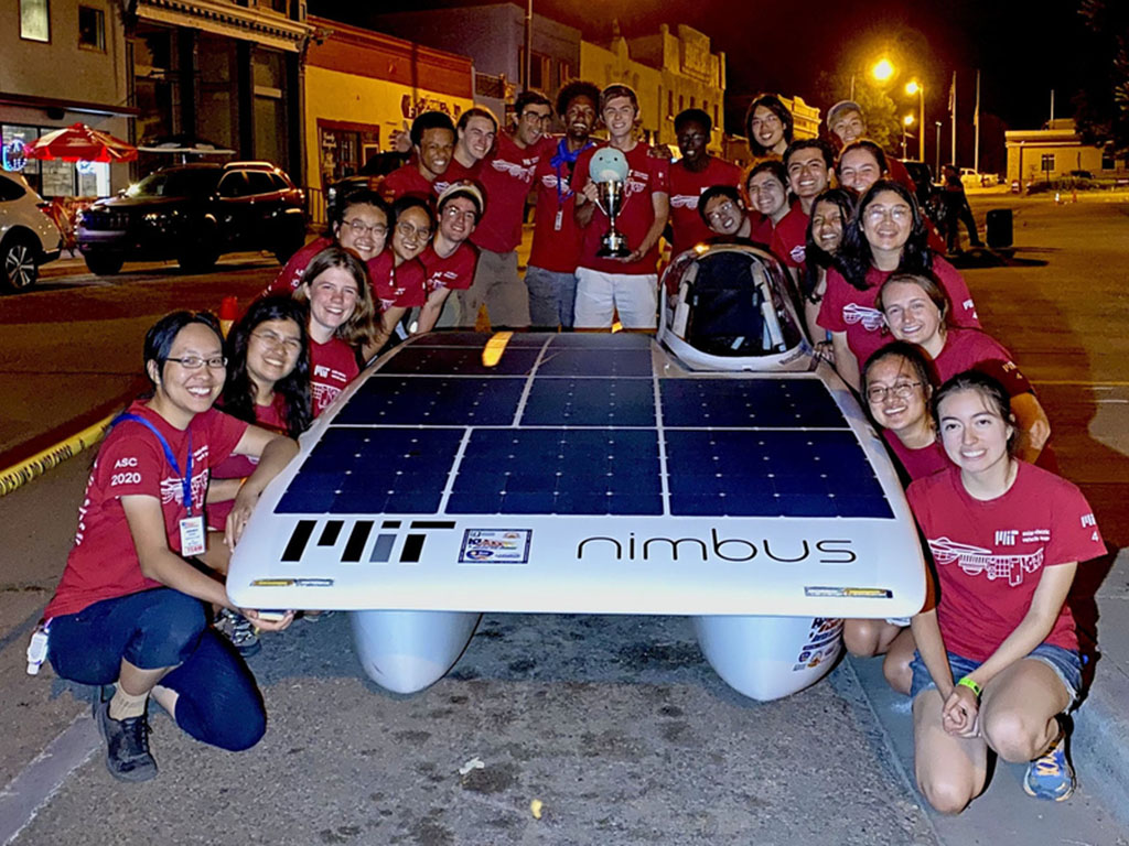 Caption:The MIT Solar Electric Vehicle Team poses with Nimbus, their solar car, after winning the 2021 American Solar Challenge.