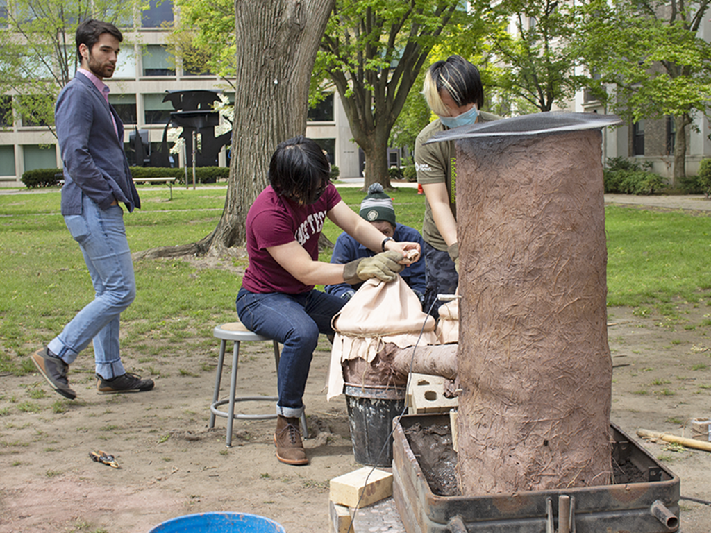 MIT students and volunteers take turns working the bellows on a mud-and-straw furnace in the style of the Mossi people of Burkina Faso.